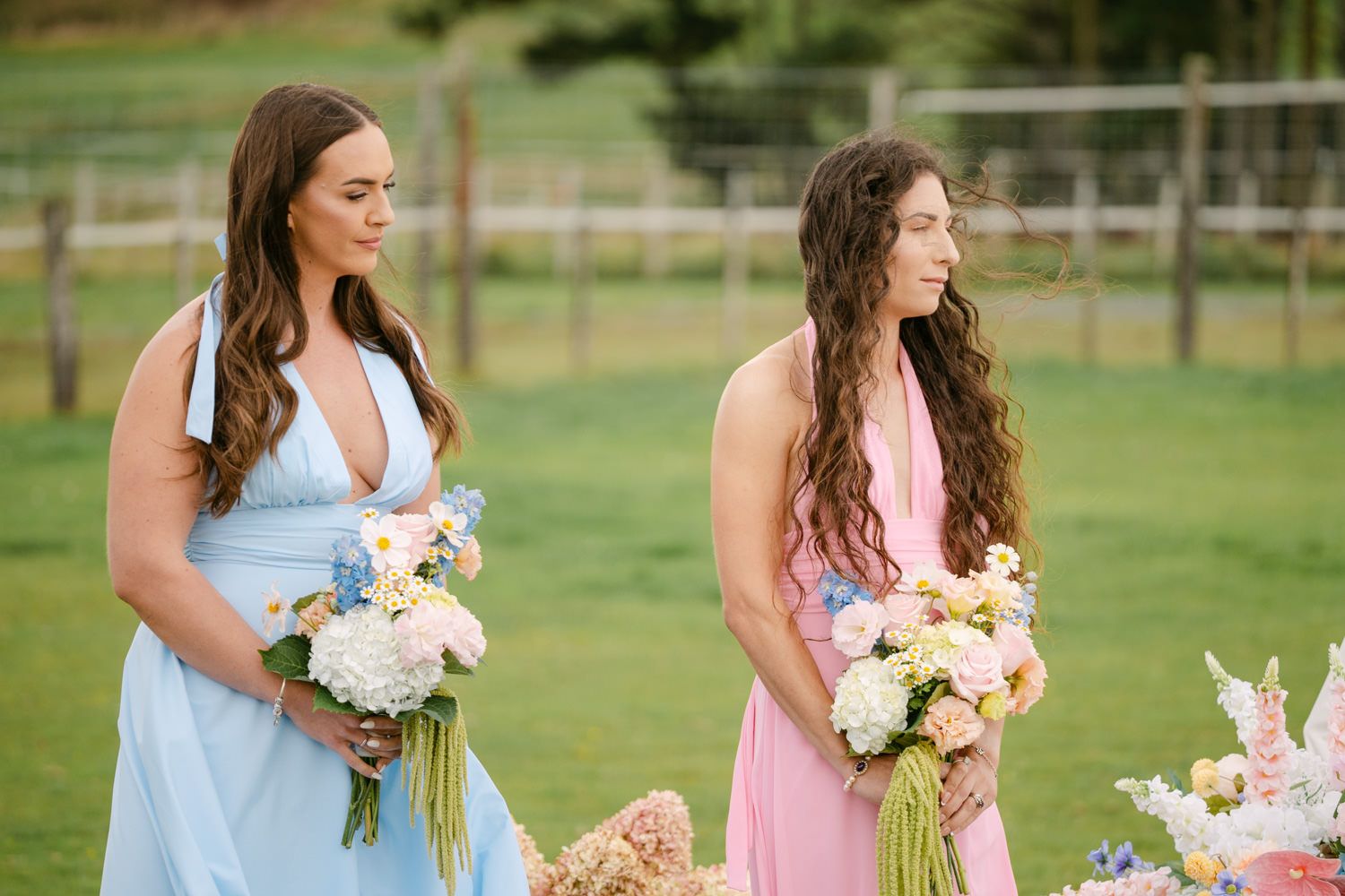 Two bridesmaids in blue and pink dresses holding floral bouquets at an outdoor wedding ceremony.