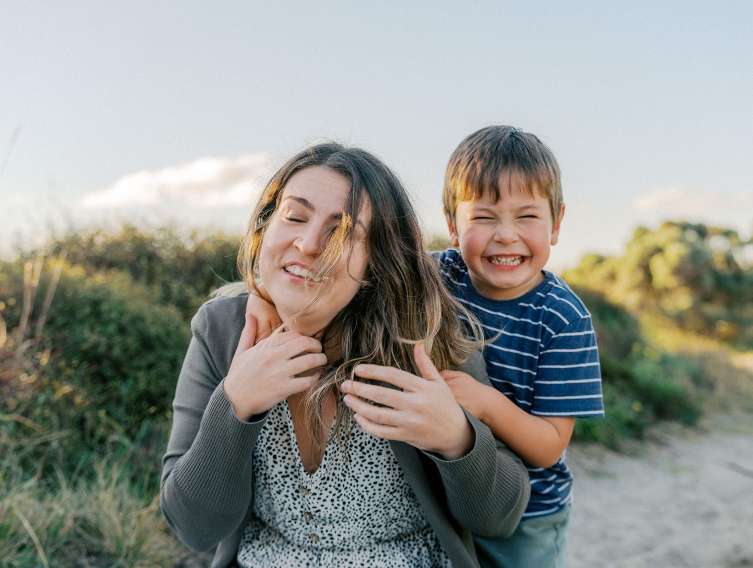 A joyful mother and young boy laughing outdoors on a sunny trail, sharing a playful moment together.