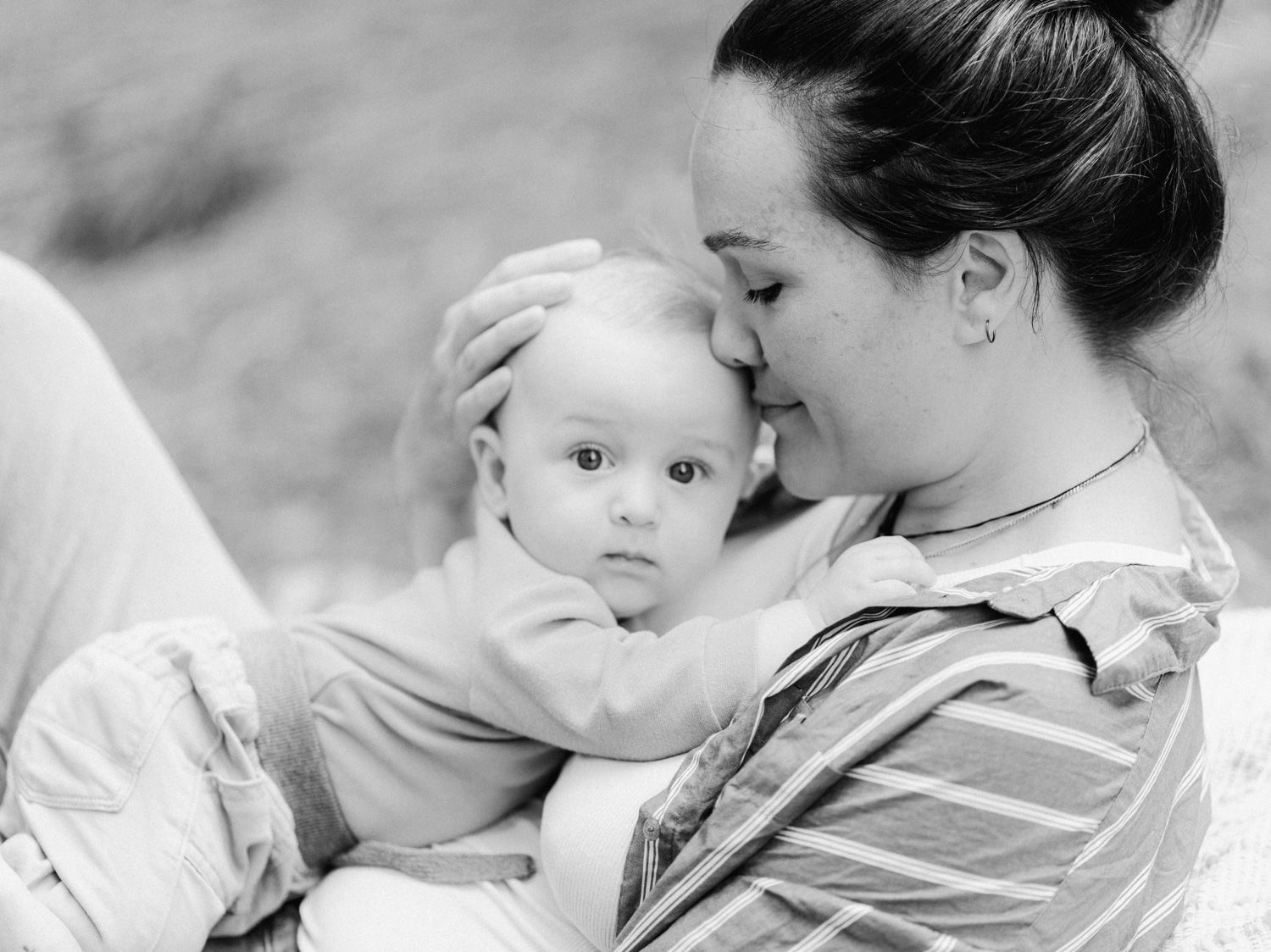 Black and white photo of a mother tenderly holding her baby close, touching foreheads in a loving outdoor moment.