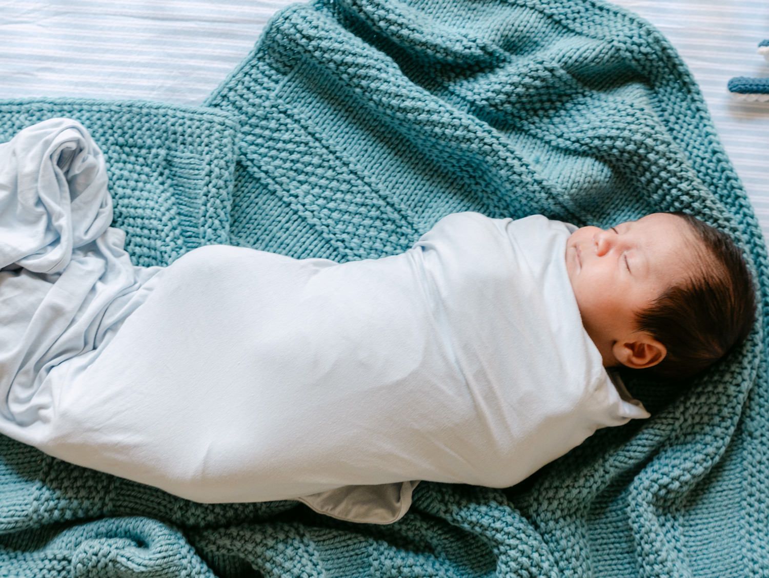 Swaddled newborn baby sleeping on a teal knit blanket with tiny feet peeking out.