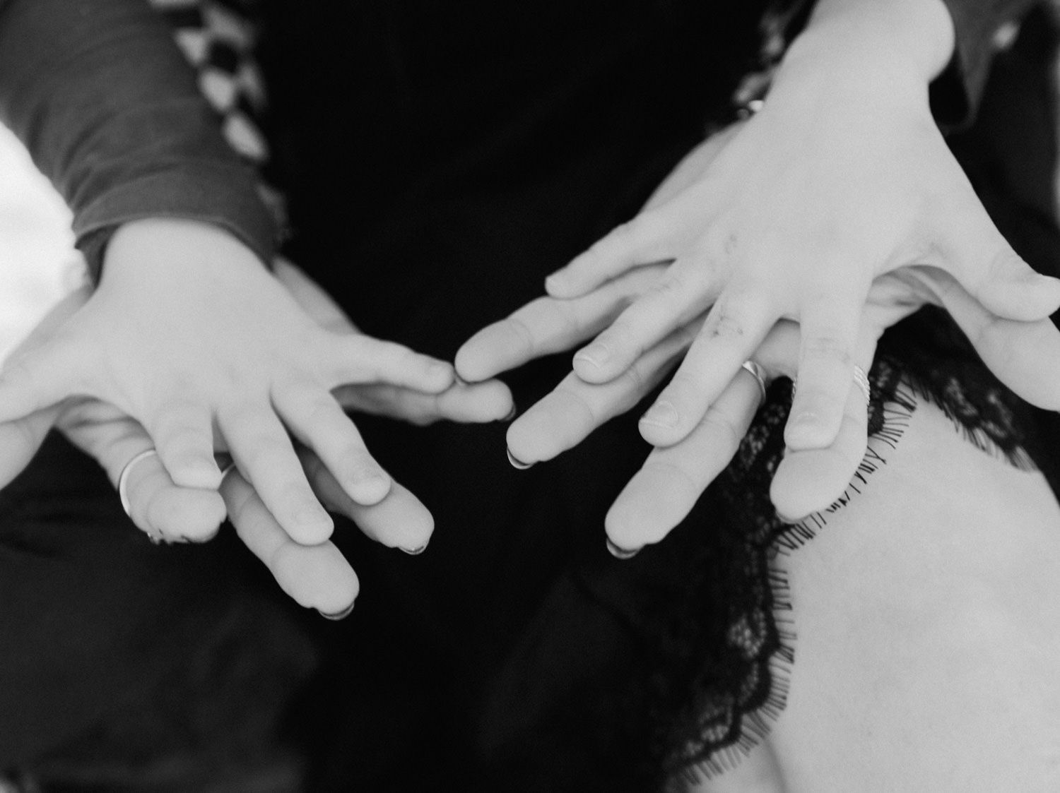 Close-up black and white photo of three pairs of hands touching fingertips together.