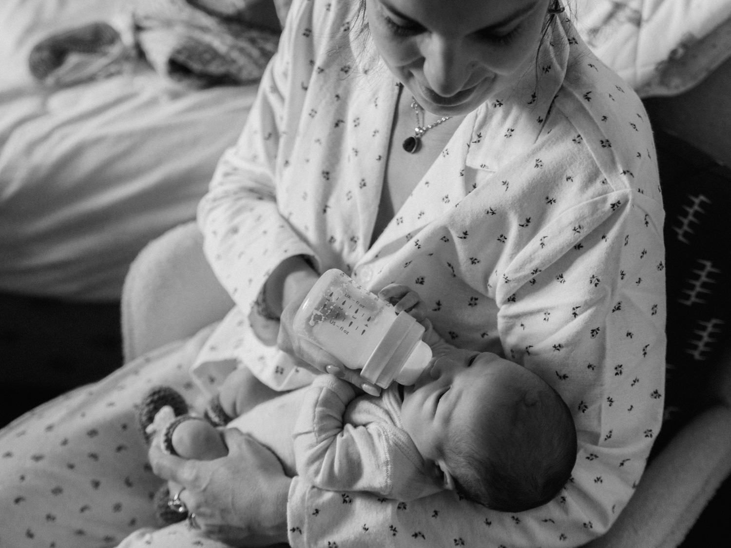 Black and white photo of a mother in hospital gown bottle feeding her newborn baby after birth.