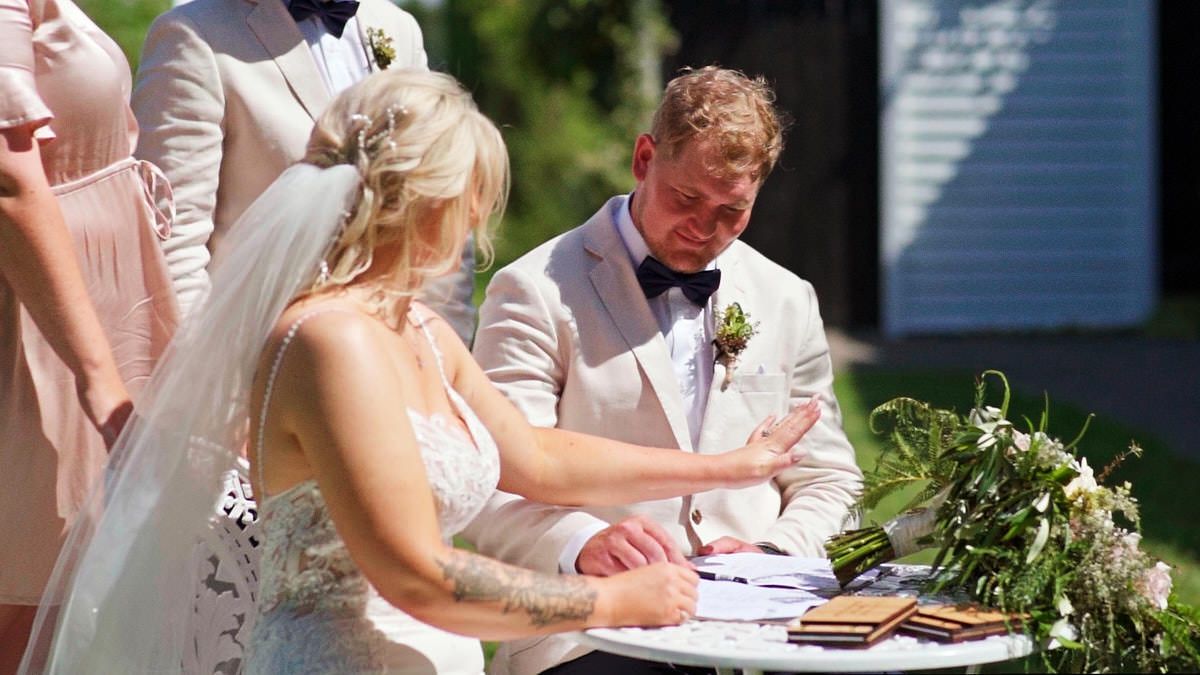 Bride and groom signing wedding registry documents outdoors at elegant ceremony with floral arrangements.