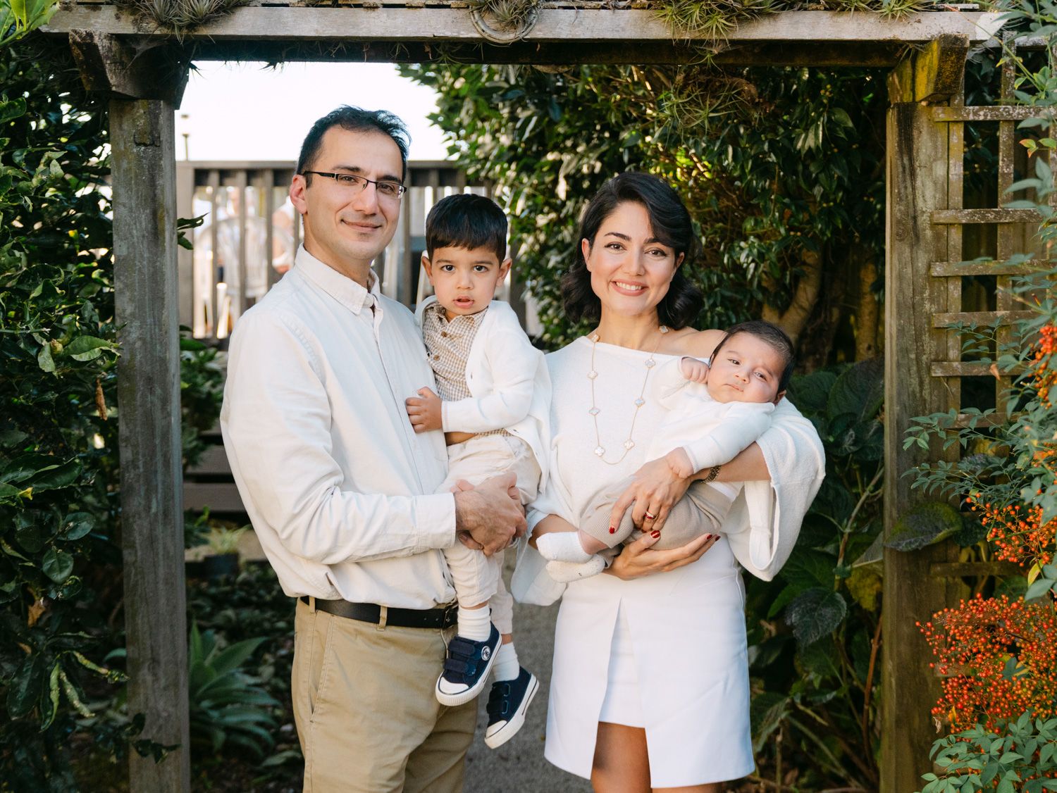 Happy family of four posing outdoors under a wooden arbor surrounded by lush greenery.