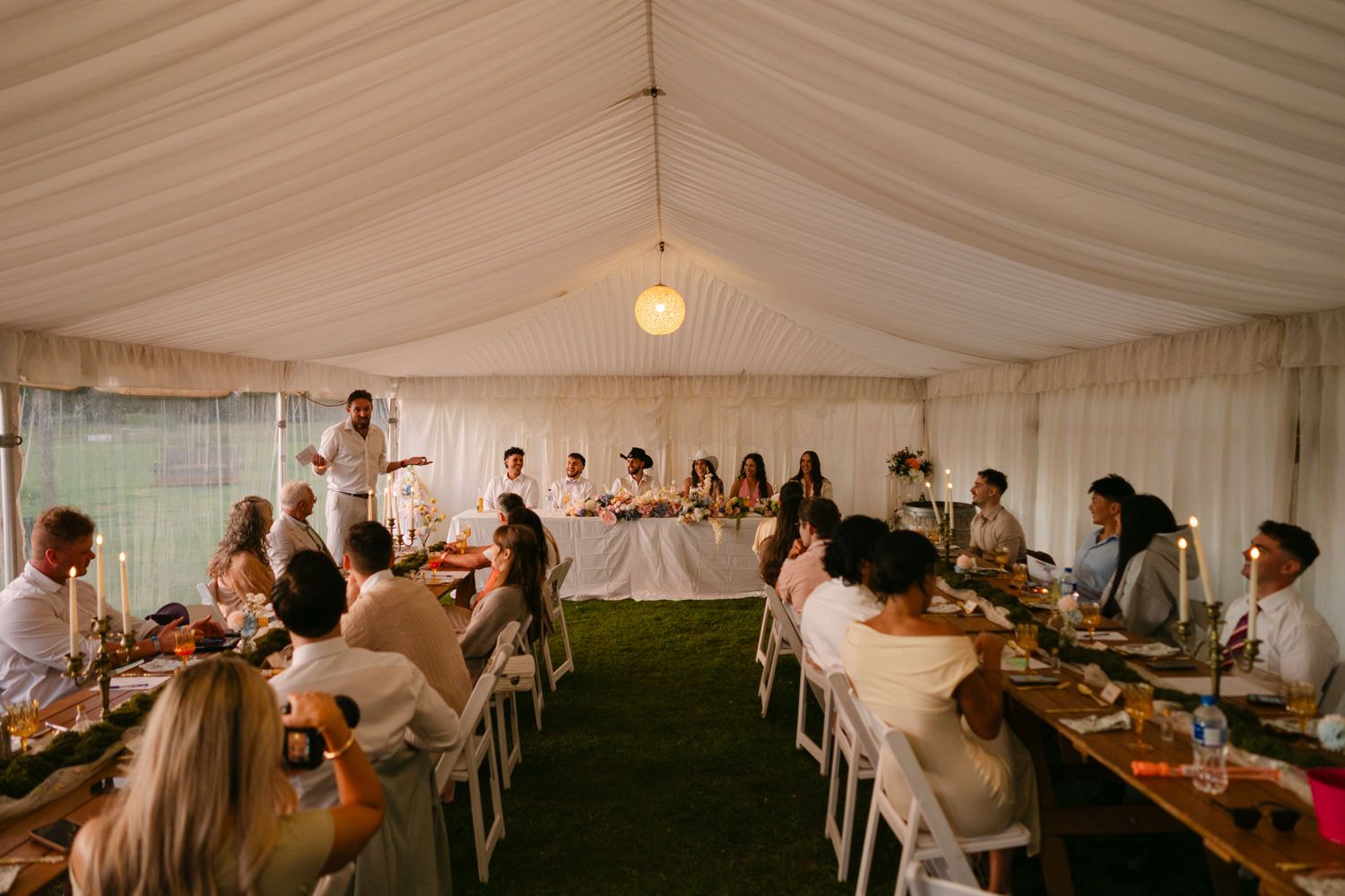 Elegant wedding reception under a white marquee tent with guests seated at long decorated tables.
