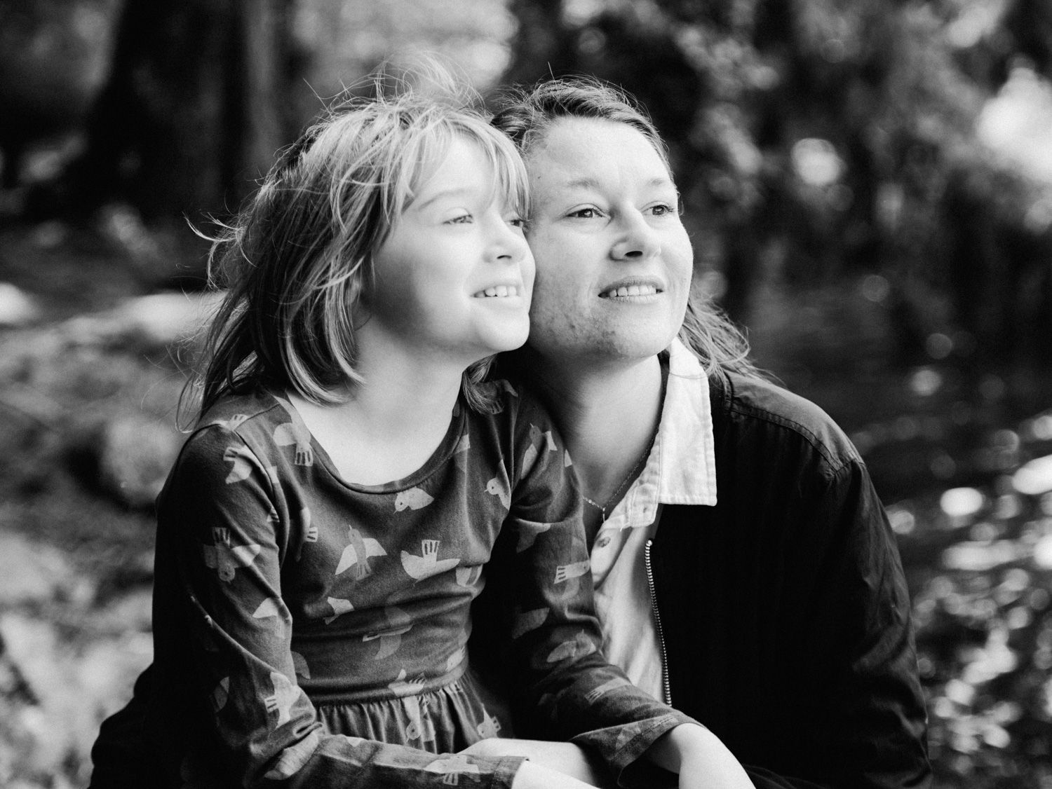 Black and white portrait of a young girl and older child smiling together outdoors among trees.