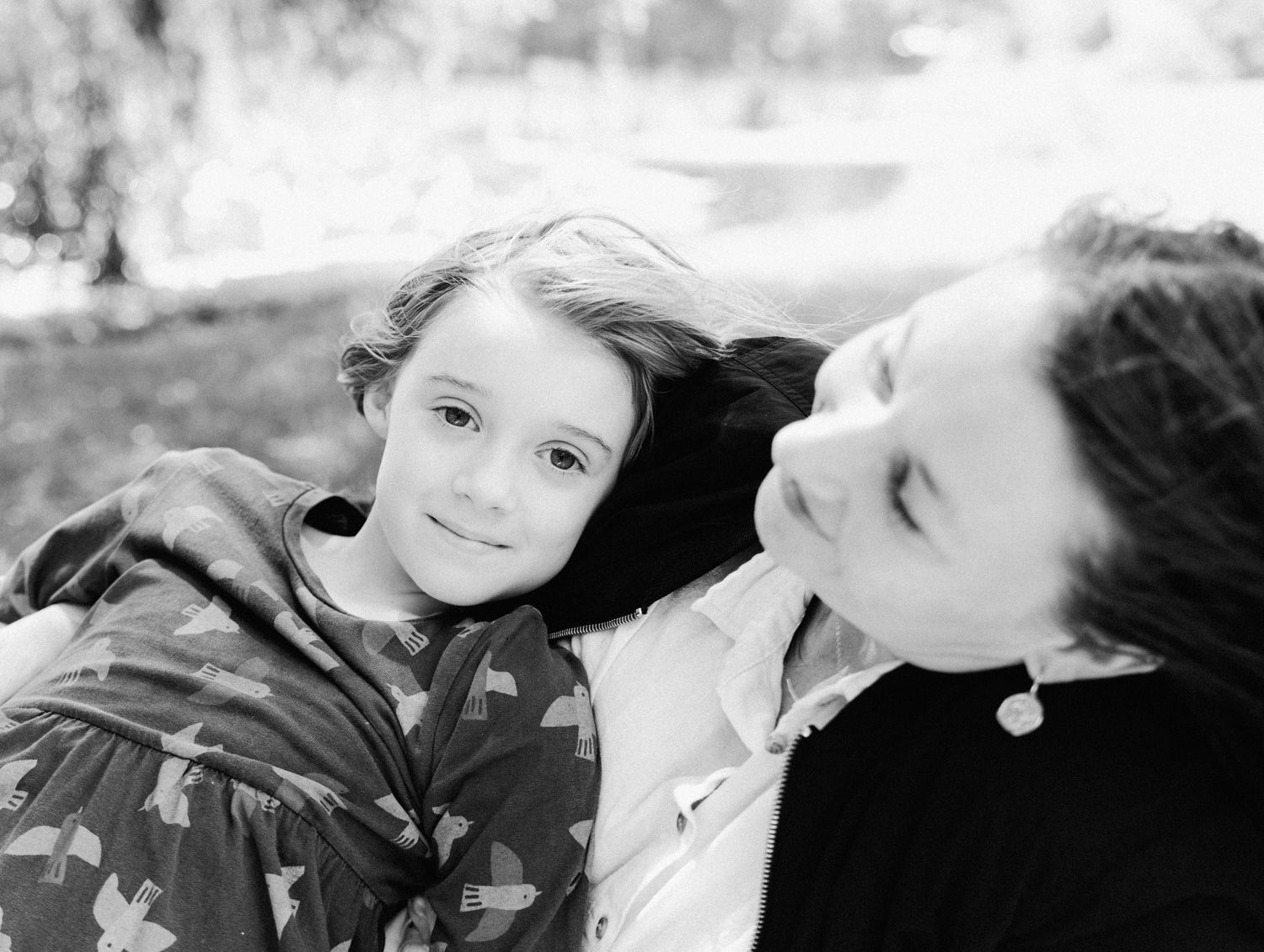 Black and white photo of a young child leaning on an adult, sharing a tender moment outdoors.