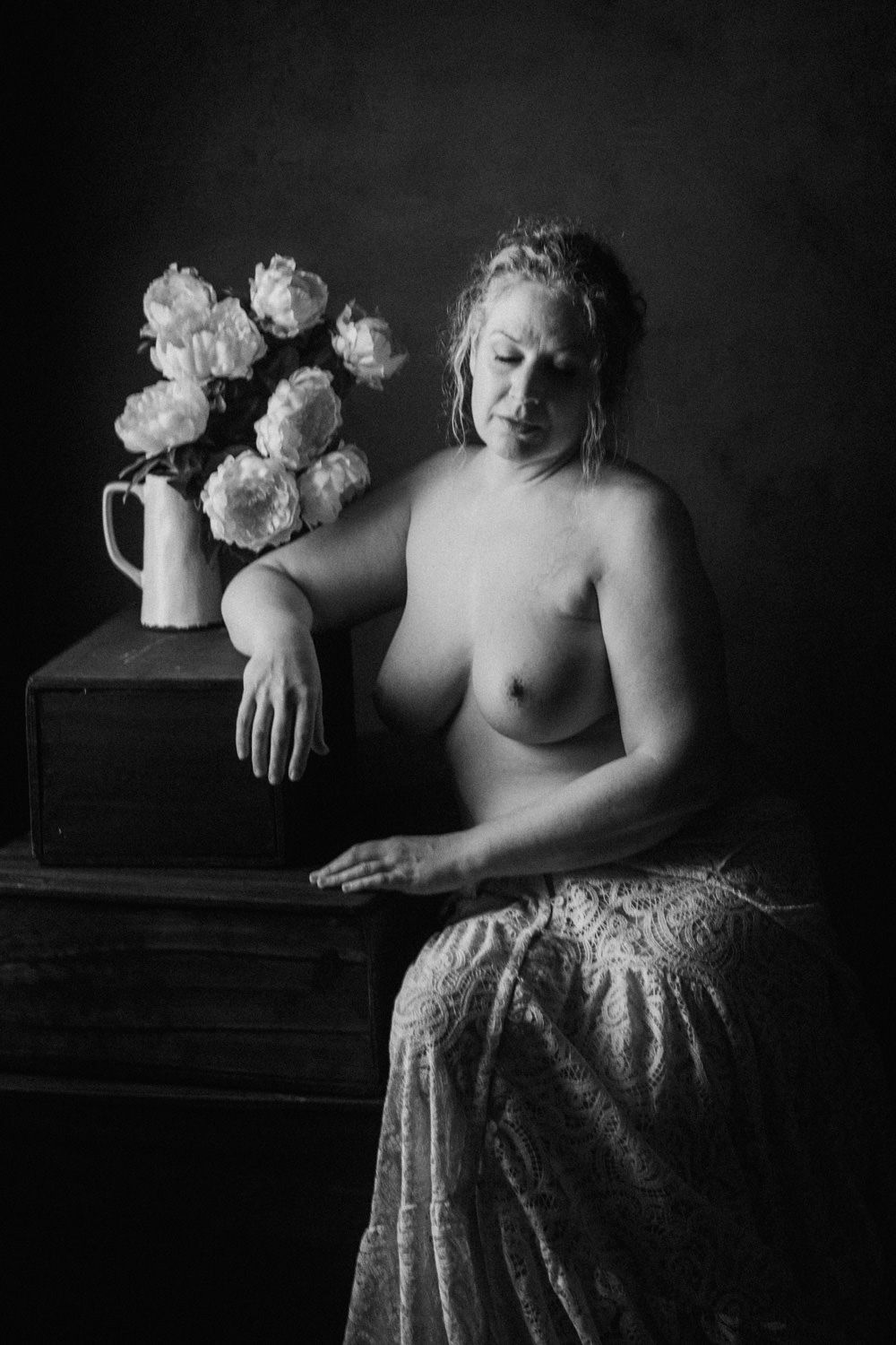 Black and white fine art portrait of a woman seated beside a vase of flowers, styled in classical painting aesthetic.