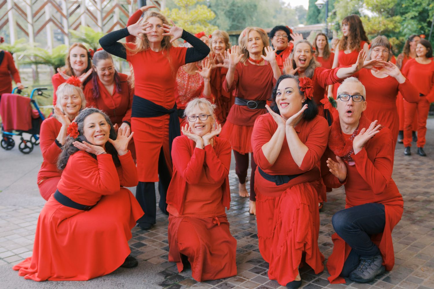 Large group of women in matching red outfits posing playfully outdoors for a fun group photo.