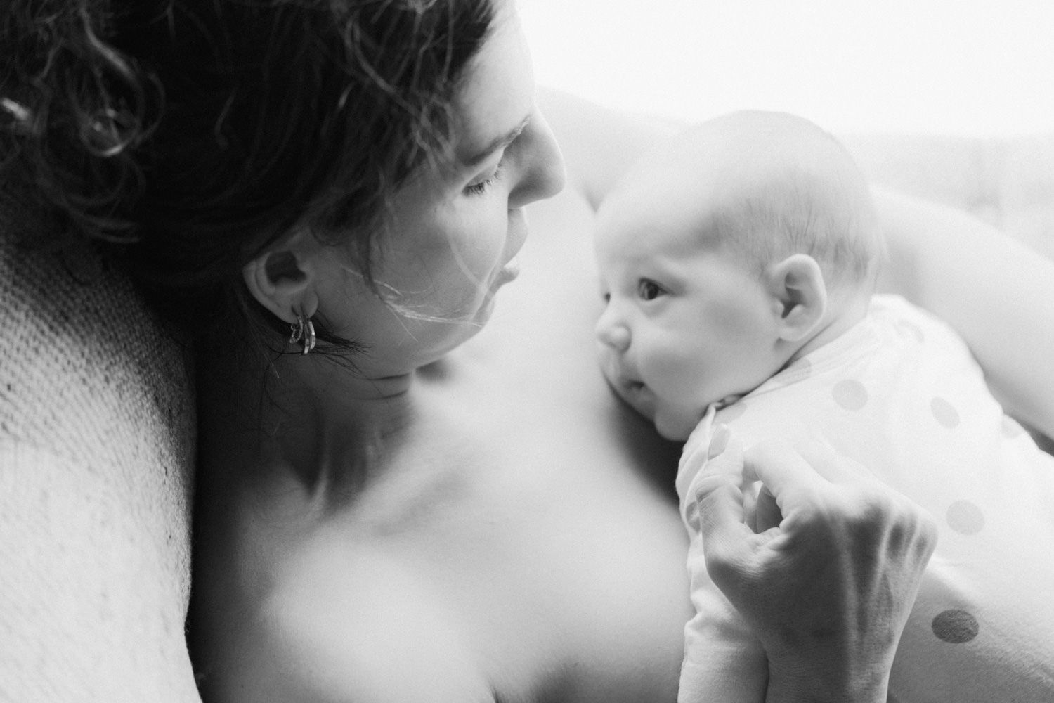 Black and white photo of a mother tenderly gazing at her newborn baby, sharing an intimate bonding moment.