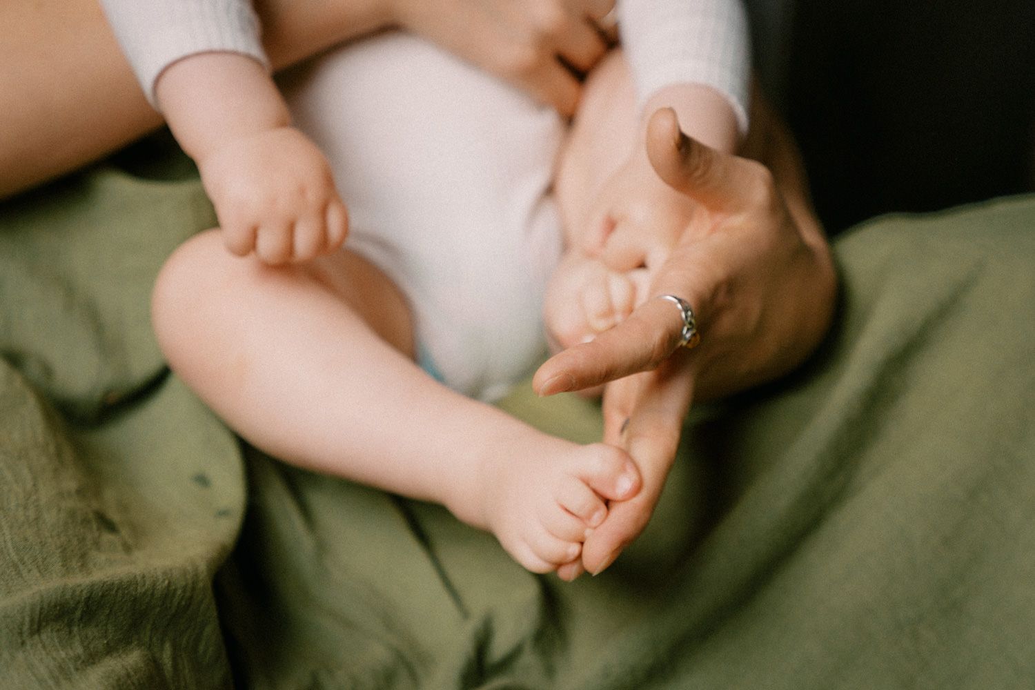 Close-up of a parent's hands gently holding a newborn baby's tiny feet on a soft green blanket.