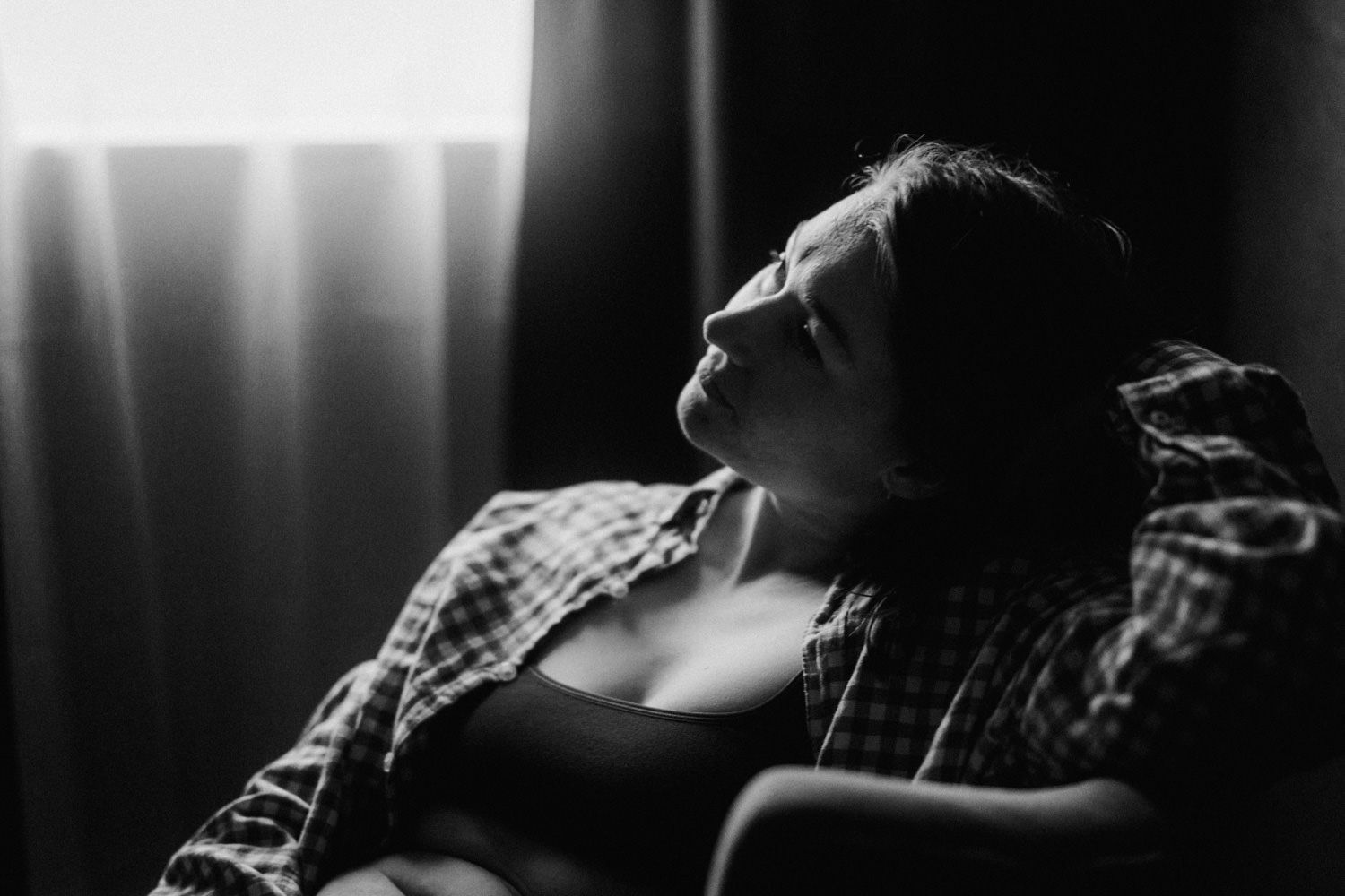 Black and white photo of a woman reclining in a chair near a curtained window, eyes closed in peaceful repose.