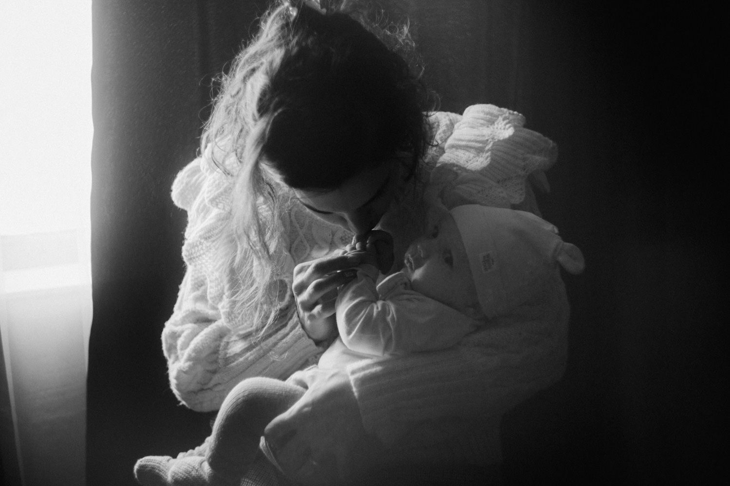 Black and white photo of a young girl curled up by a window, hugging her knees in a contemplative pose.