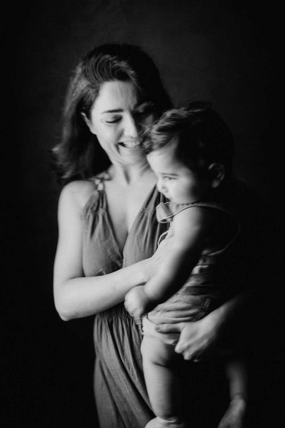 Black and white photo of a smiling mother holding her toddler child in a studio portrait.
