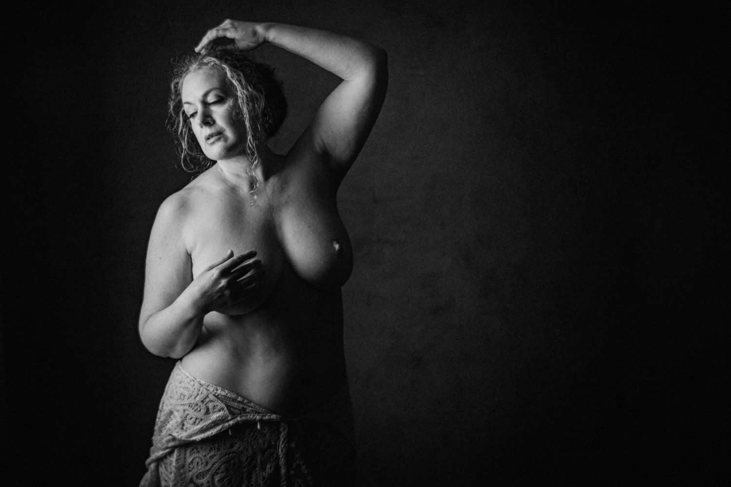 Black and white artistic boudoir portrait of a curvy woman posing gracefully with hand in hair.