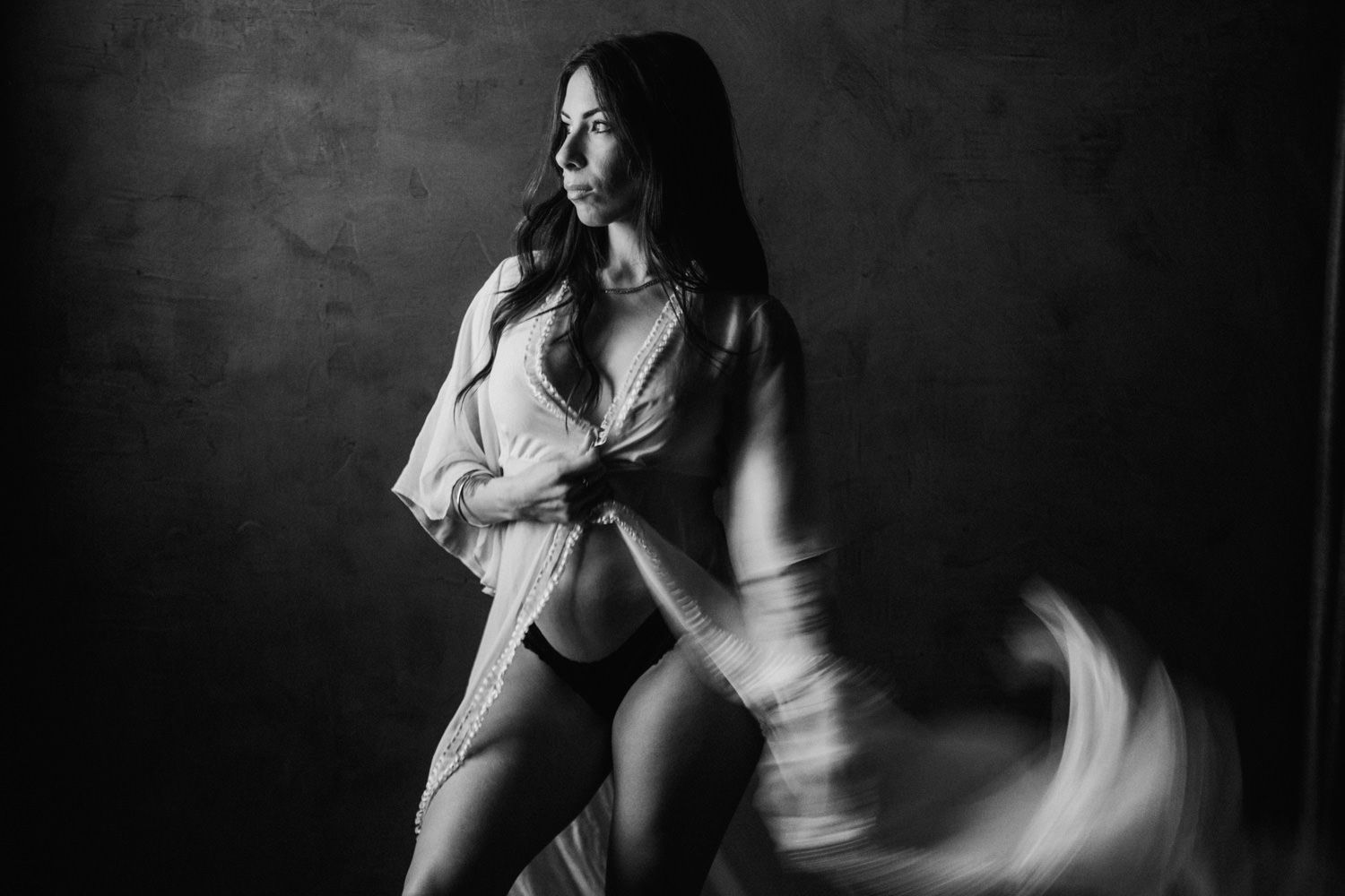 Black and white photo of a woman in an open shirt and lingerie, posing dynamically in a studio setting.
