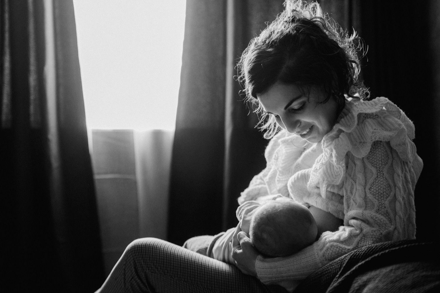 Black and white photo of a young mother tenderly cradling her newborn baby by a window.