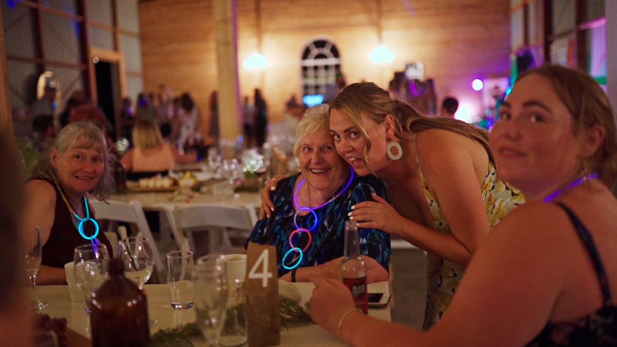 Women smiling and posing together at an elegant indoor wedding reception dinner with glowing lights.
