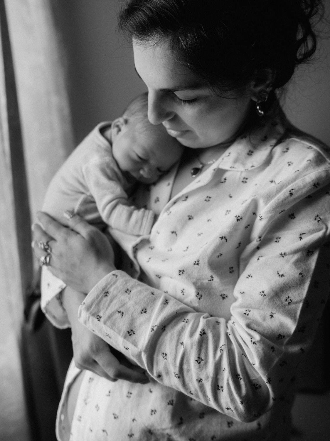 Black and white photo of a mother tenderly cradling her sleeping newborn baby close to her chest.