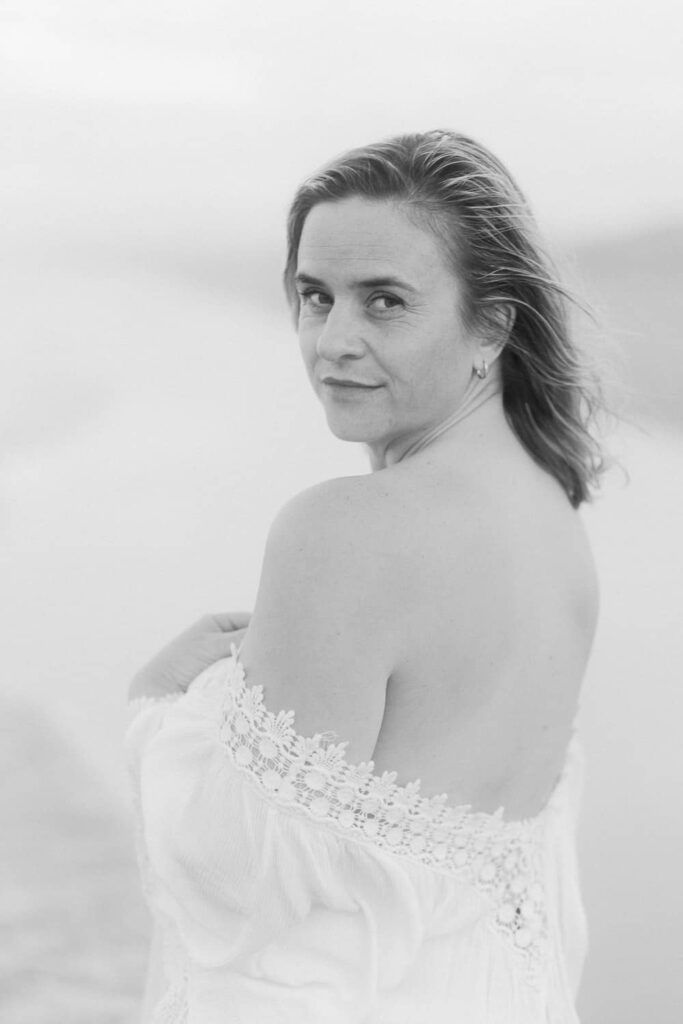Black and white portrait of a woman in an off-shoulder lace dress, looking back over her shoulder outdoors.