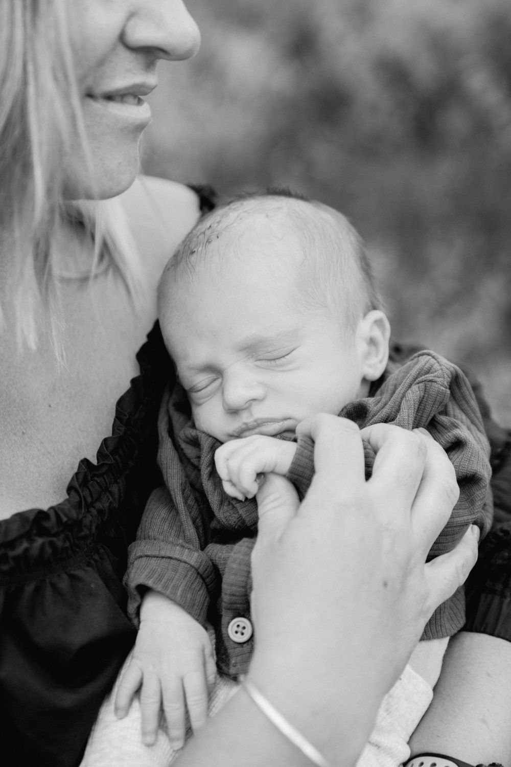 Black and white photo of a smiling mother cradling her sleeping newborn baby outdoors.