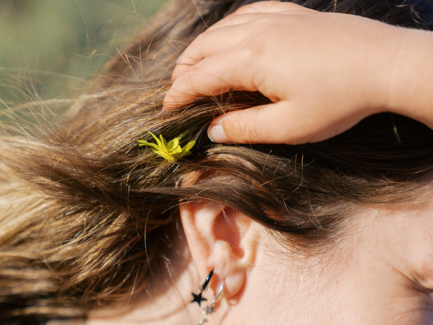 A child places a small yellow flower in a woman's hair near her ear with star tattoos.