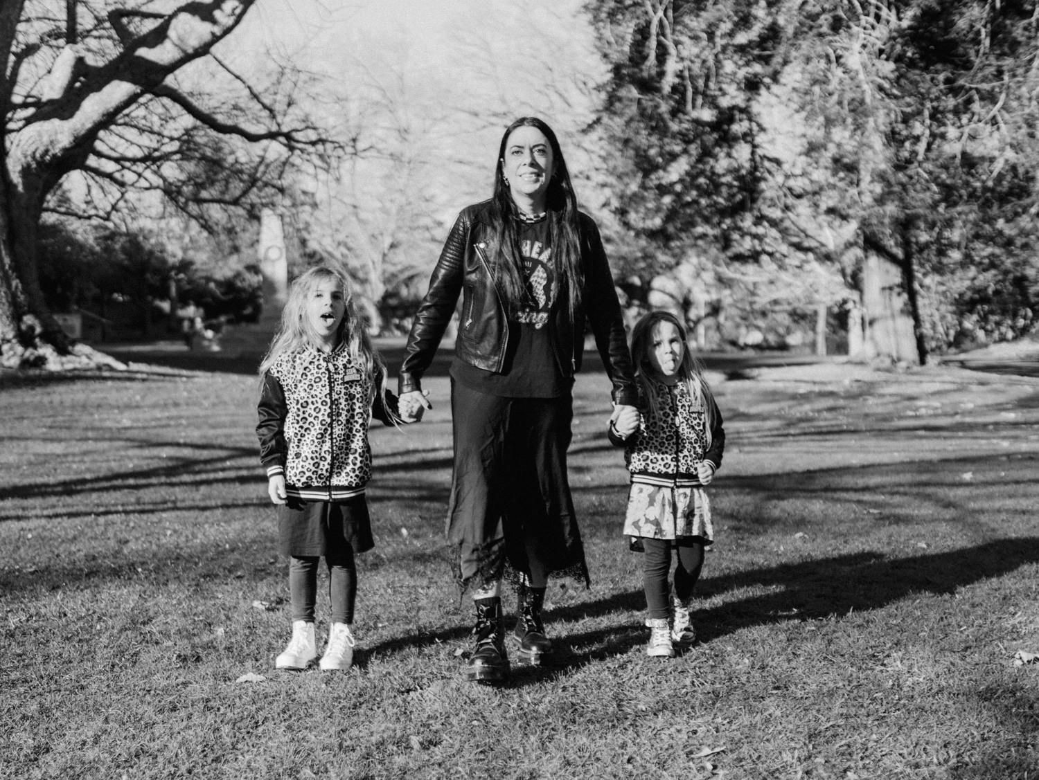 Black and white photo of a woman holding hands with two young girls walking through a park.