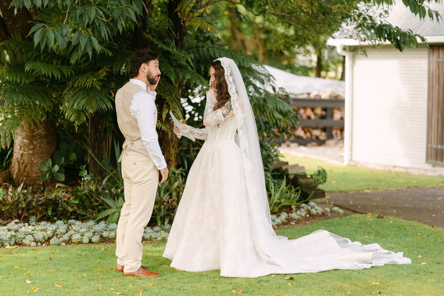 A bride and groom share a romantic moment outdoors on a lush green lawn during their wedding ceremony.