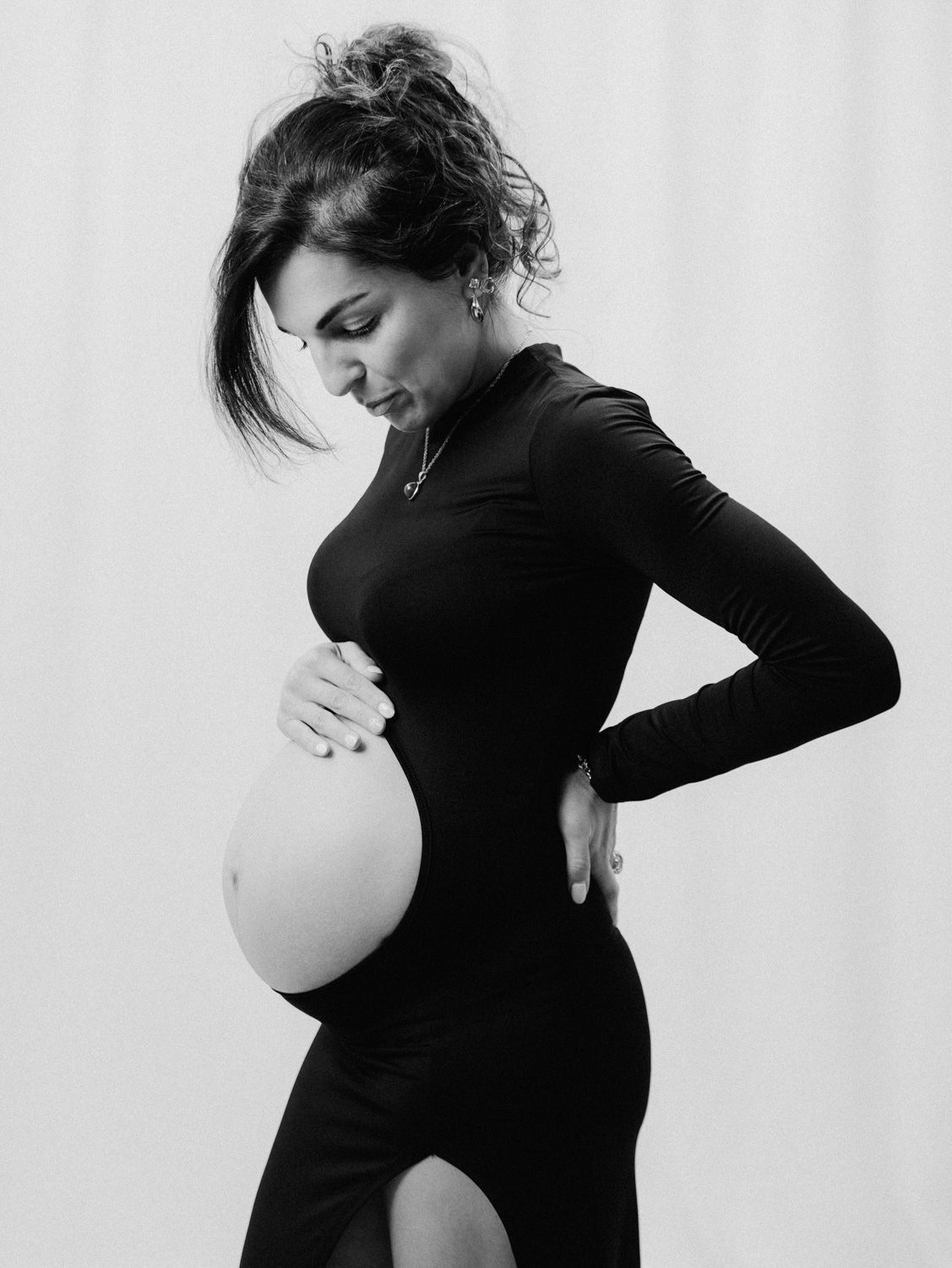 Black and white maternity photo of a pregnant woman in a black dress cradling her baby bump.