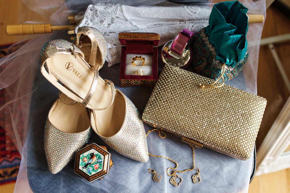 Gold bridal accessories flat lay featuring heels, clutch purse, ring box, earrings, necklace, and decorative brooch.