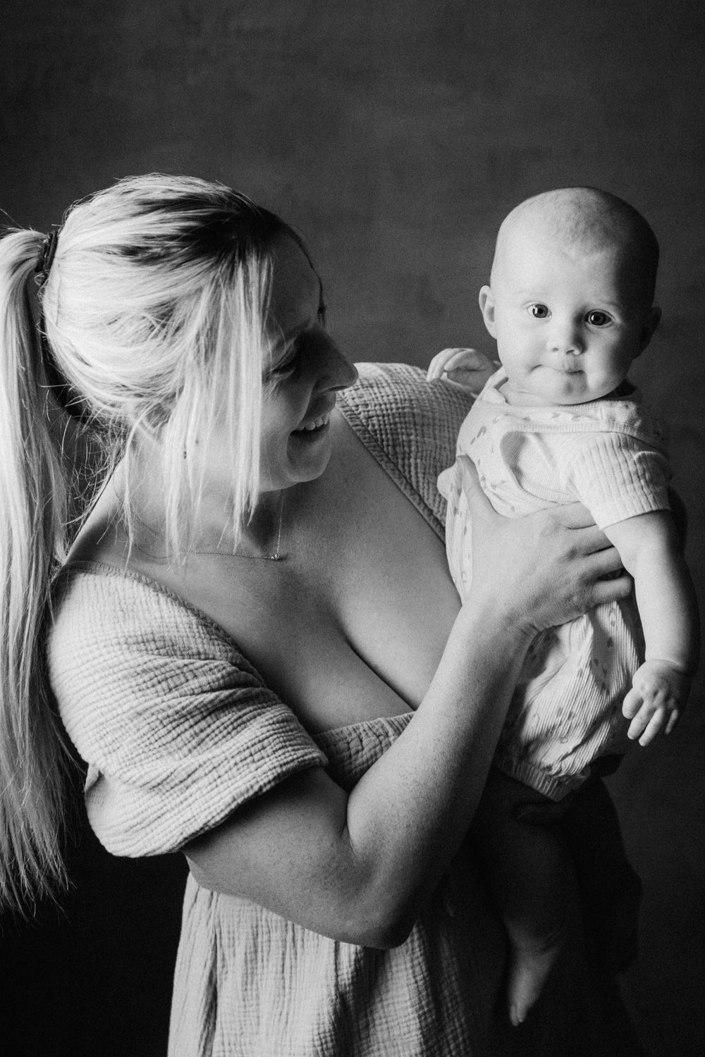 Black and white photo of a blonde mother lovingly holding her infant baby in a studio portrait.