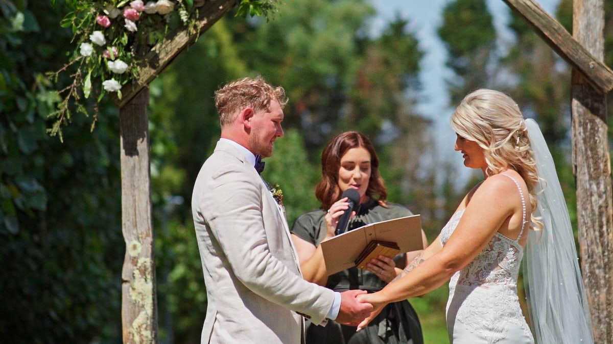 Outdoor wedding ceremony with bride and groom holding hands under a floral arch, officiant reading vows in sunny garden.