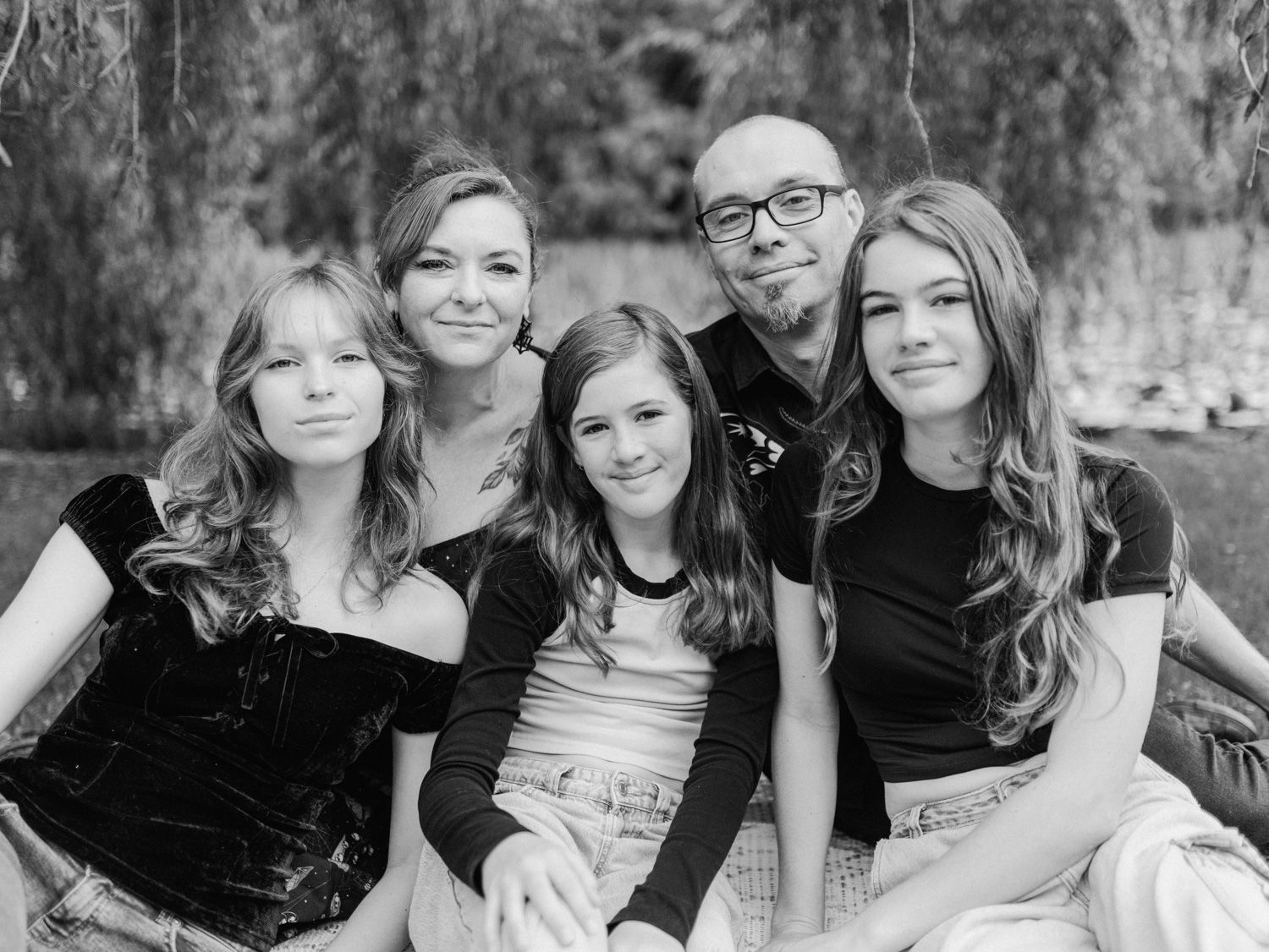 Black and white family portrait of five people sitting together outdoors near trees, smiling warmly.