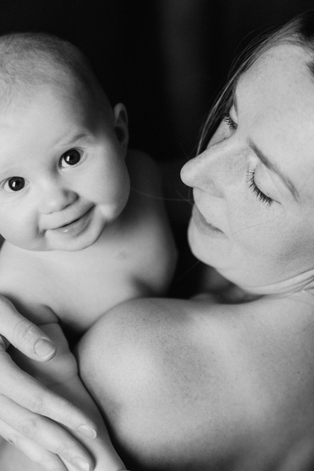 Black and white portrait of a mother tenderly holding her smiling baby close to her chest.