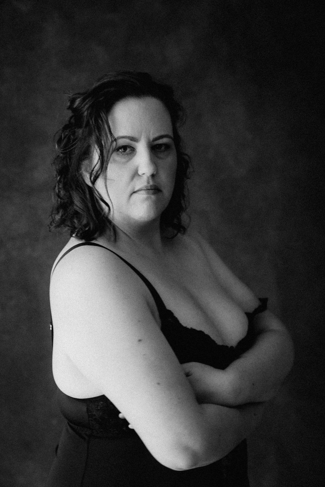 Black and white studio portrait of a woman in lingerie with arms crossed, looking directly at camera.