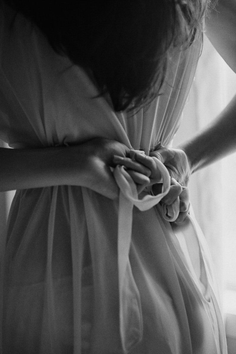 Black and white photo of hands tying a satin ribbon bow on a sheer white bridal robe.