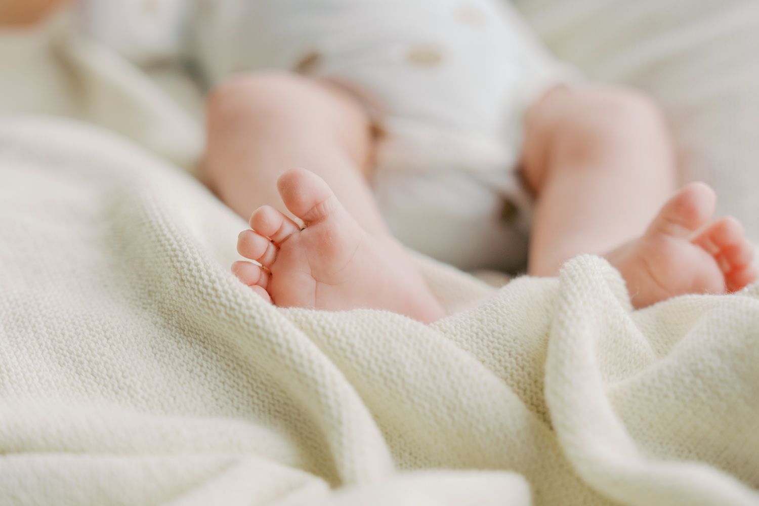 Close-up of tiny newborn baby feet resting on a soft white blanket, capturing the delicate details of infant toes.