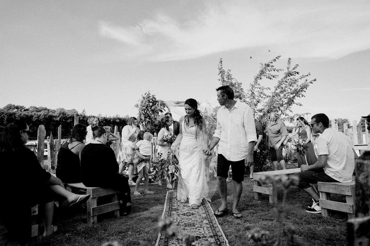 Black and white photo of newlyweds walking down the aisle at an outdoor wedding ceremony.