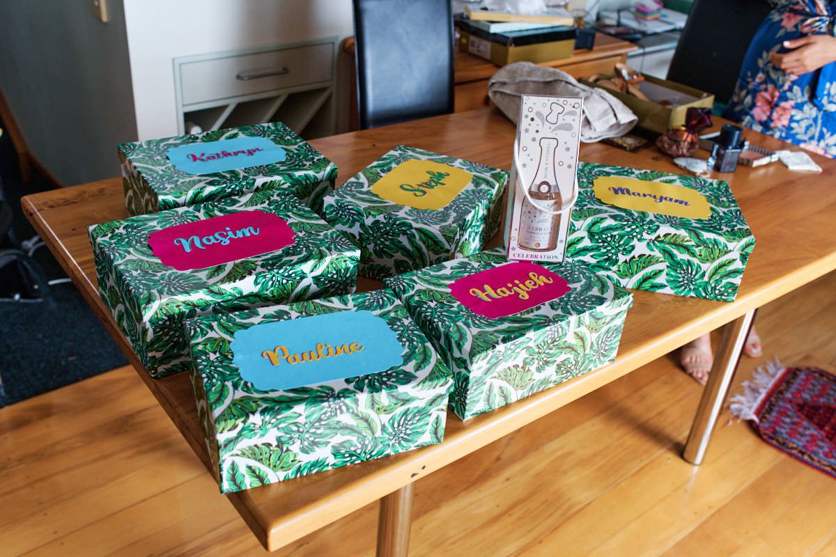 Green tropical print gift boxes with colorful name tags arranged on a wooden table.