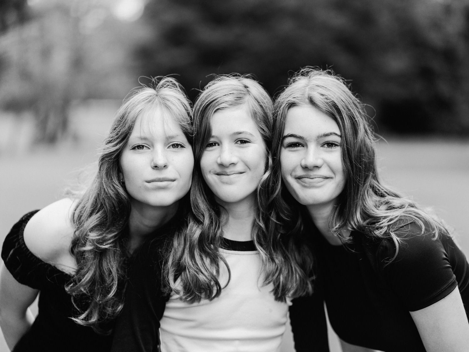 Black and white portrait of three smiling teenage girls posing together outdoors in a park setting.