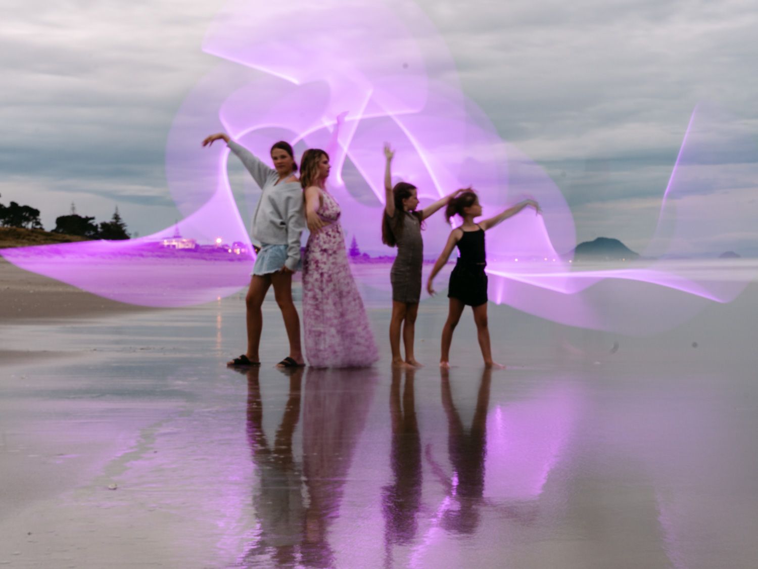 Four people posing on a beach with stunning purple light painting photography effects at dusk.