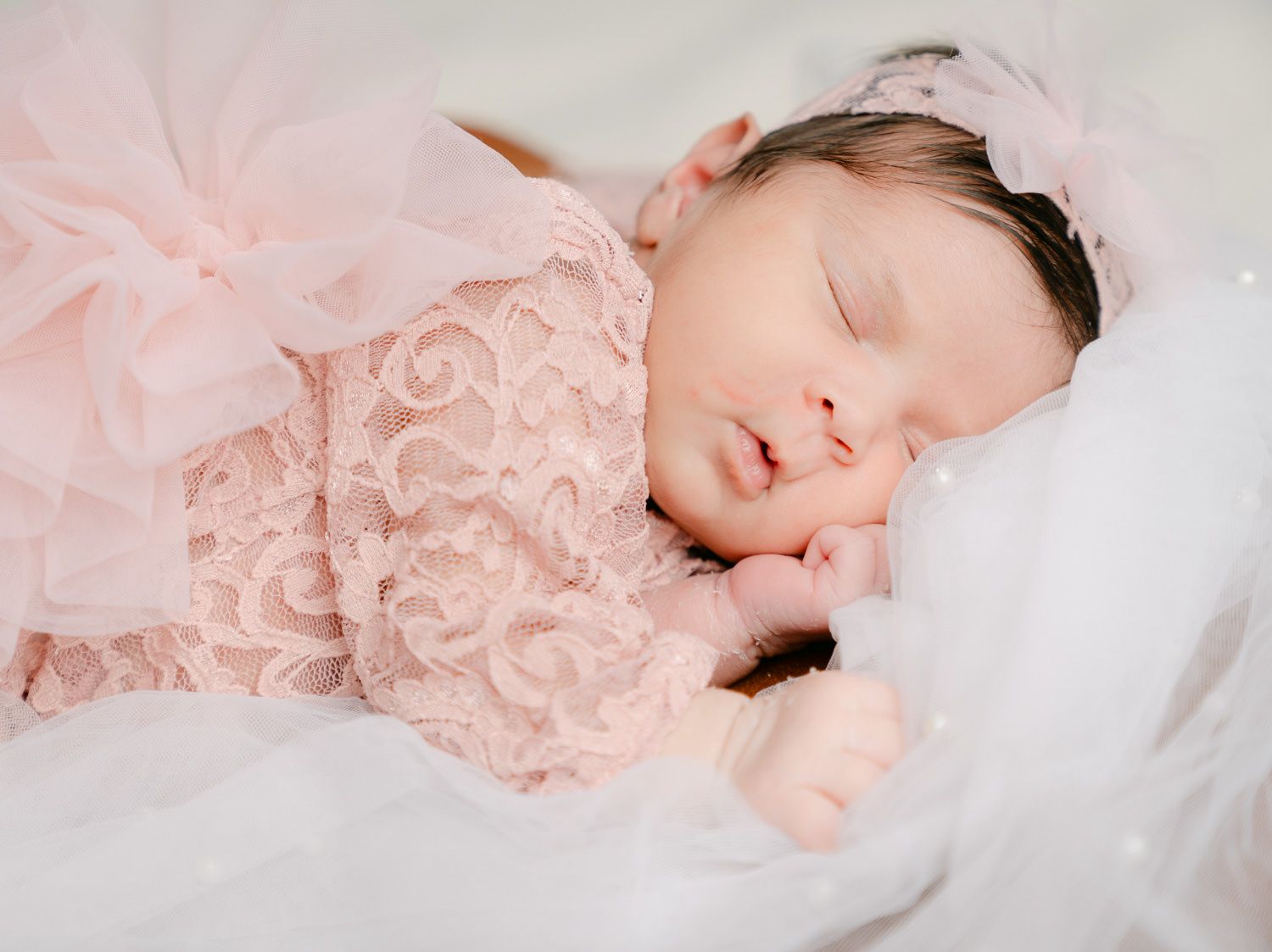 Sleeping newborn baby girl in pink lace dress and headband, peaceful infant portrait photography.