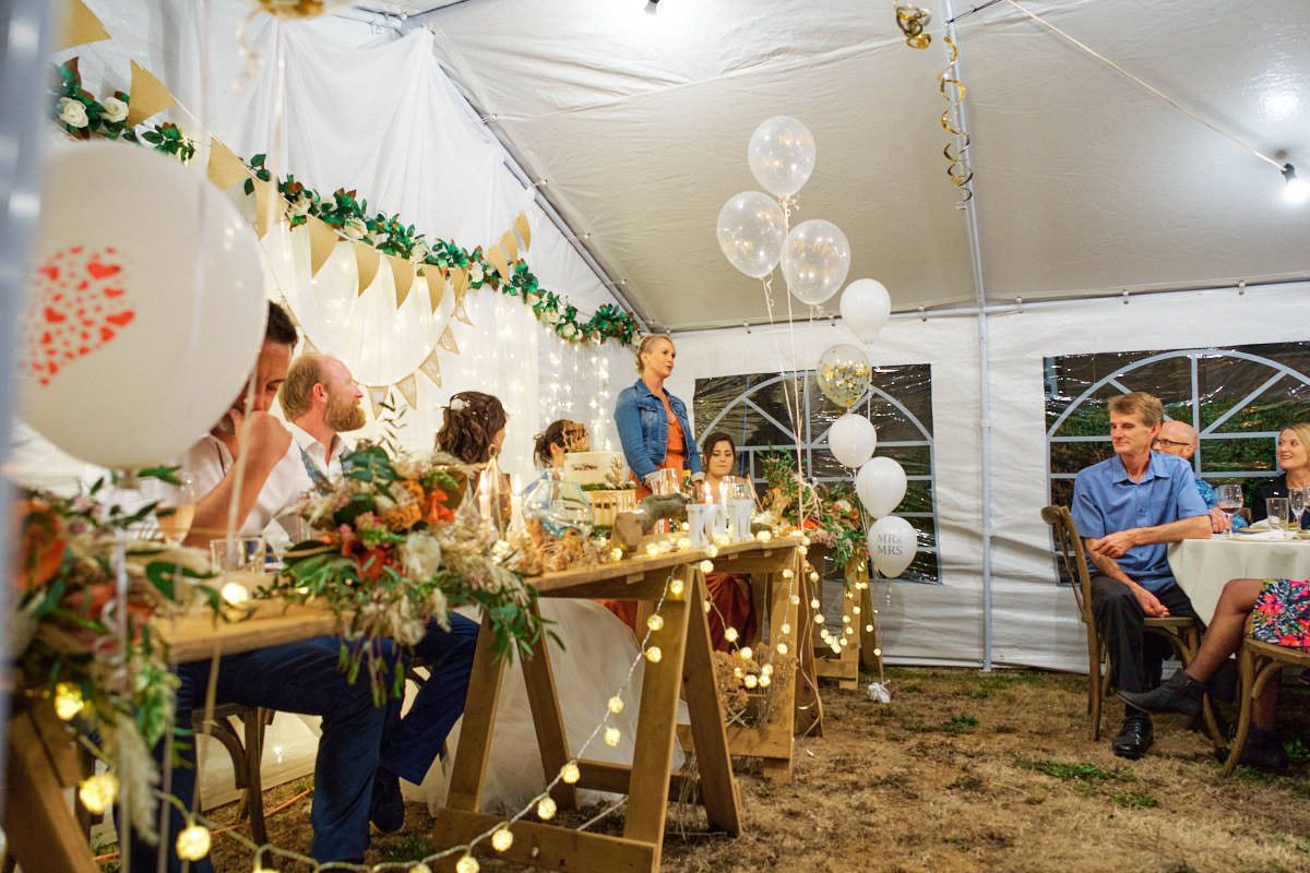 Family gathering under a decorated tent with fairy lights, balloons, and greenery garlands at a festive outdoor party.