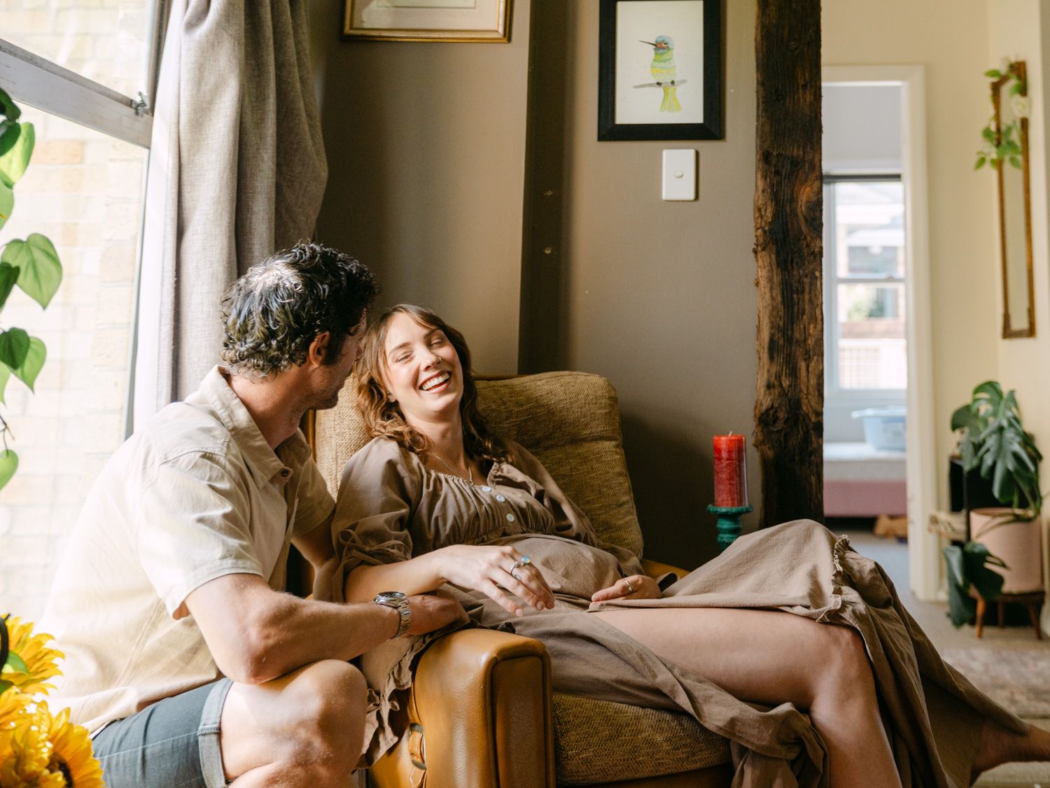 A happy couple laughing and relaxing together in a cozy armchair by a sunlit window at home.