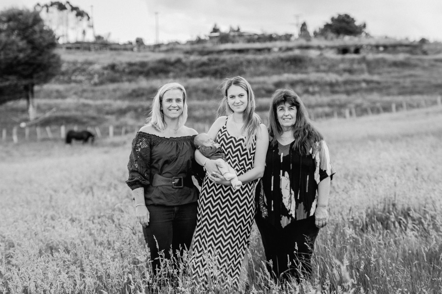 Three women smiling together in a field, black and white outdoor portrait photography.