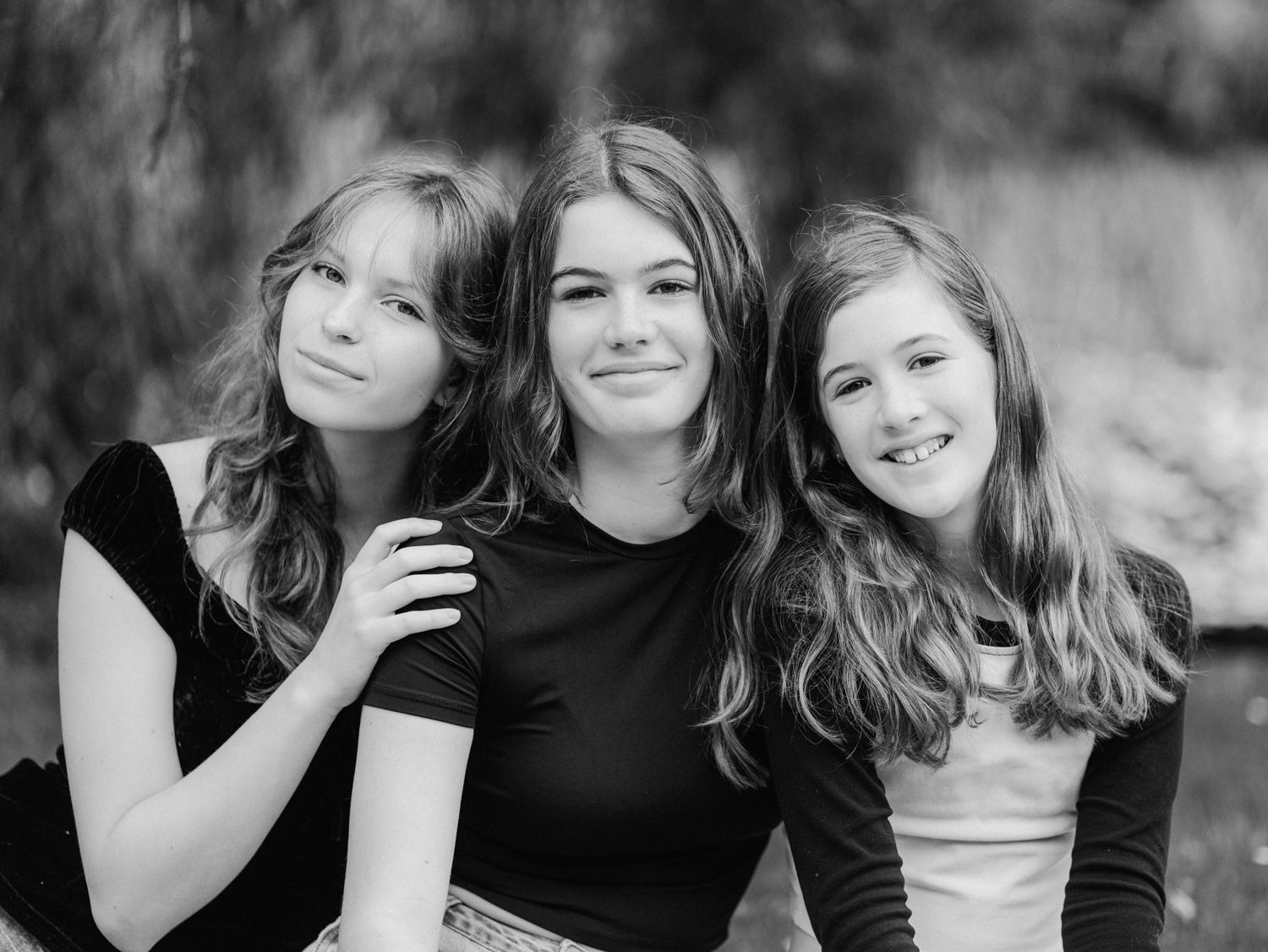 Black and white portrait of three smiling teenage girls posing together outdoors in a park setting.