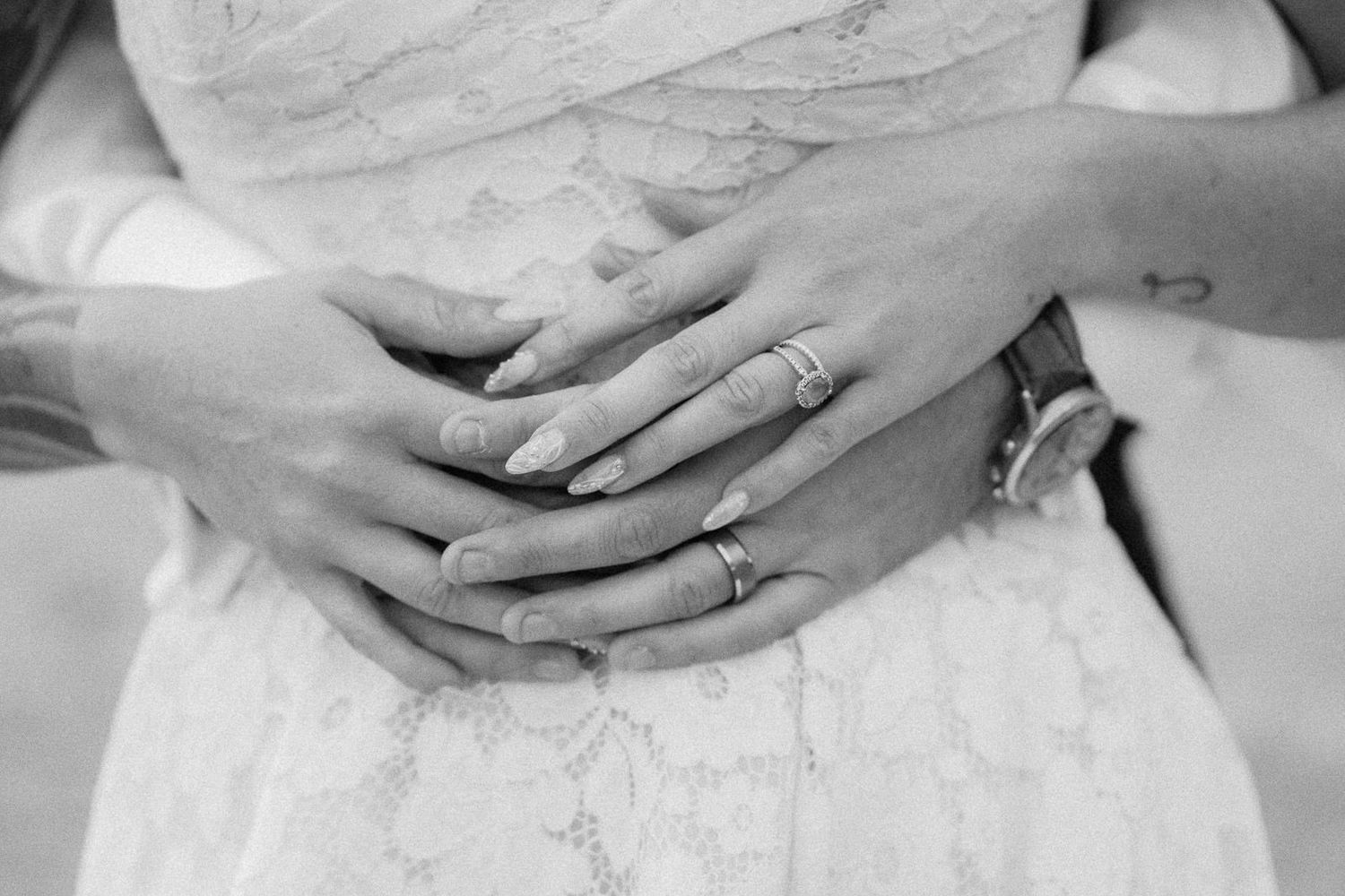 Black and white photo of couple holding hands showing wedding rings in lace wedding dress.