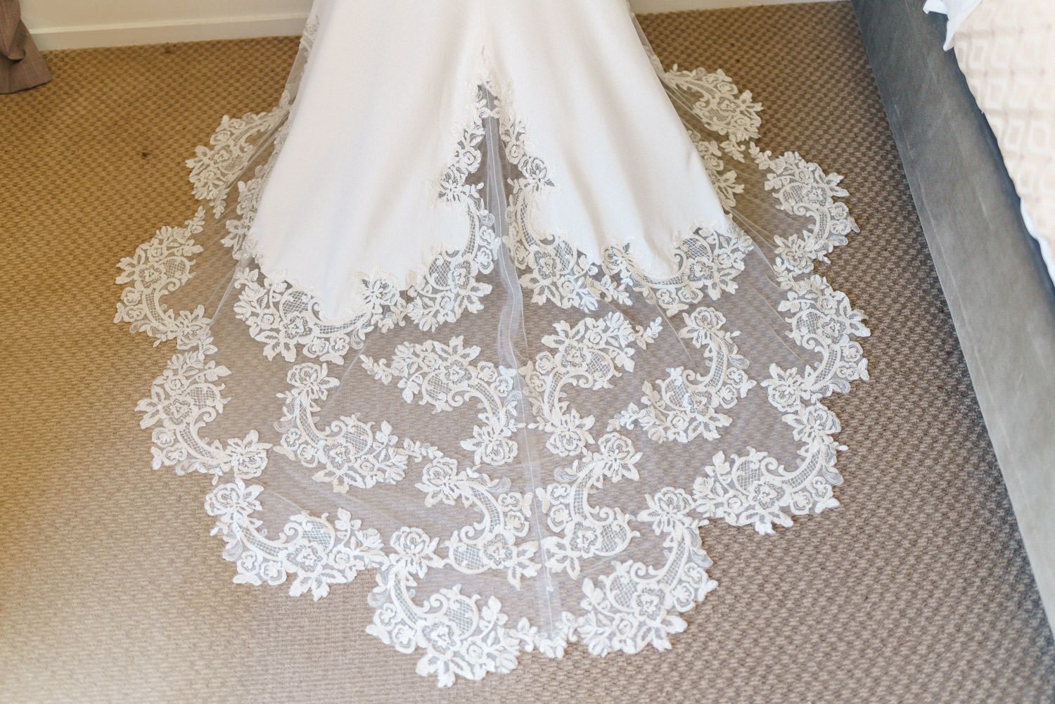 Elegant white wedding dress with intricate lace cathedral train spread on carpet.