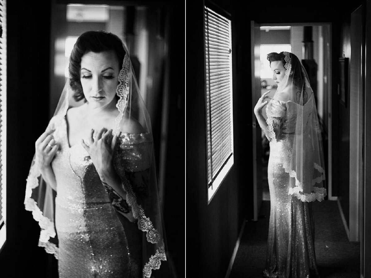 Black and white bridal portrait of elegant woman in sequin gown and lace veil posing near window.