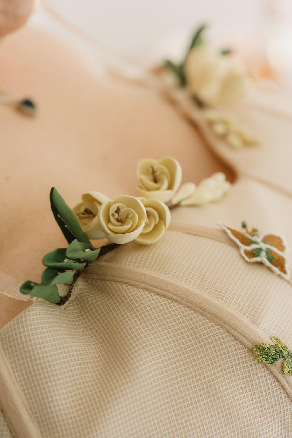 Close-up of delicate cream roses boutonniere with green leaves on a beige textured wedding dress.